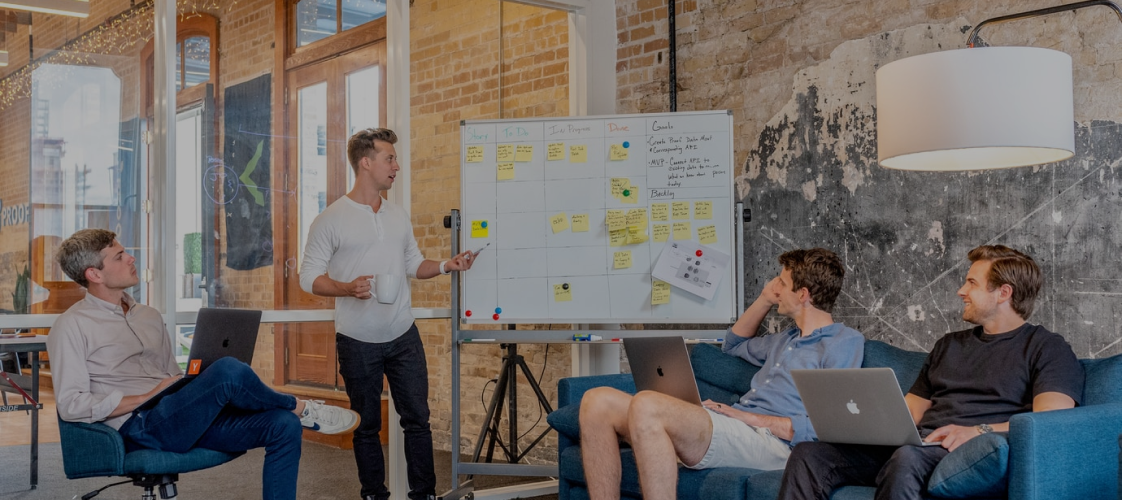 A man presents ideas on a whiteboard to three colleagues